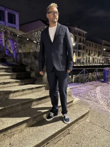 Christopher Webster on stone steps at night, in a dark jacket, white shirt, and navy sneakers.
