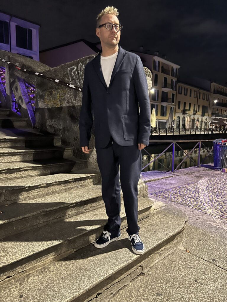 Christopher Webster on stone steps at night, in a dark jacket, white shirt, and navy sneakers.