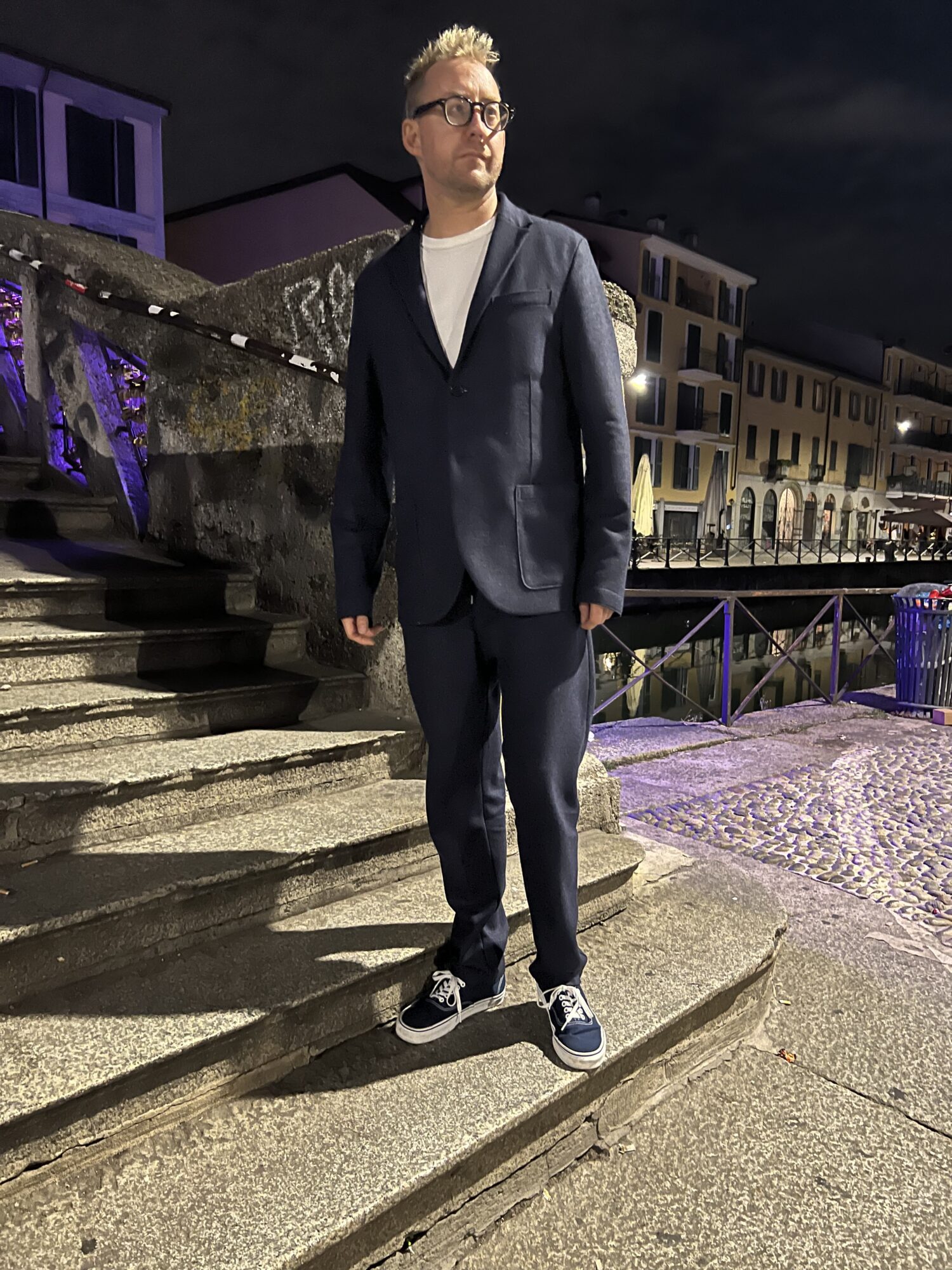 Christopher Webster on stone steps at night, in a dark jacket, white shirt, and navy sneakers.