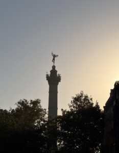 The July Column at Place de la Bastille, its gilded winged figure silhouetted against a pale evening sky above dark trees.