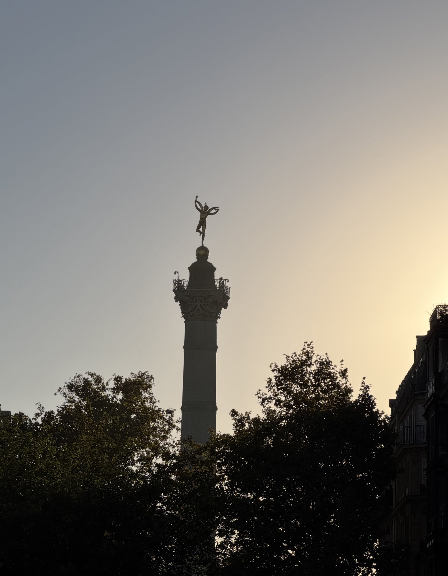 The July Column at Place de la Bastille, its gilded winged figure silhouetted against a pale evening sky above dark trees.