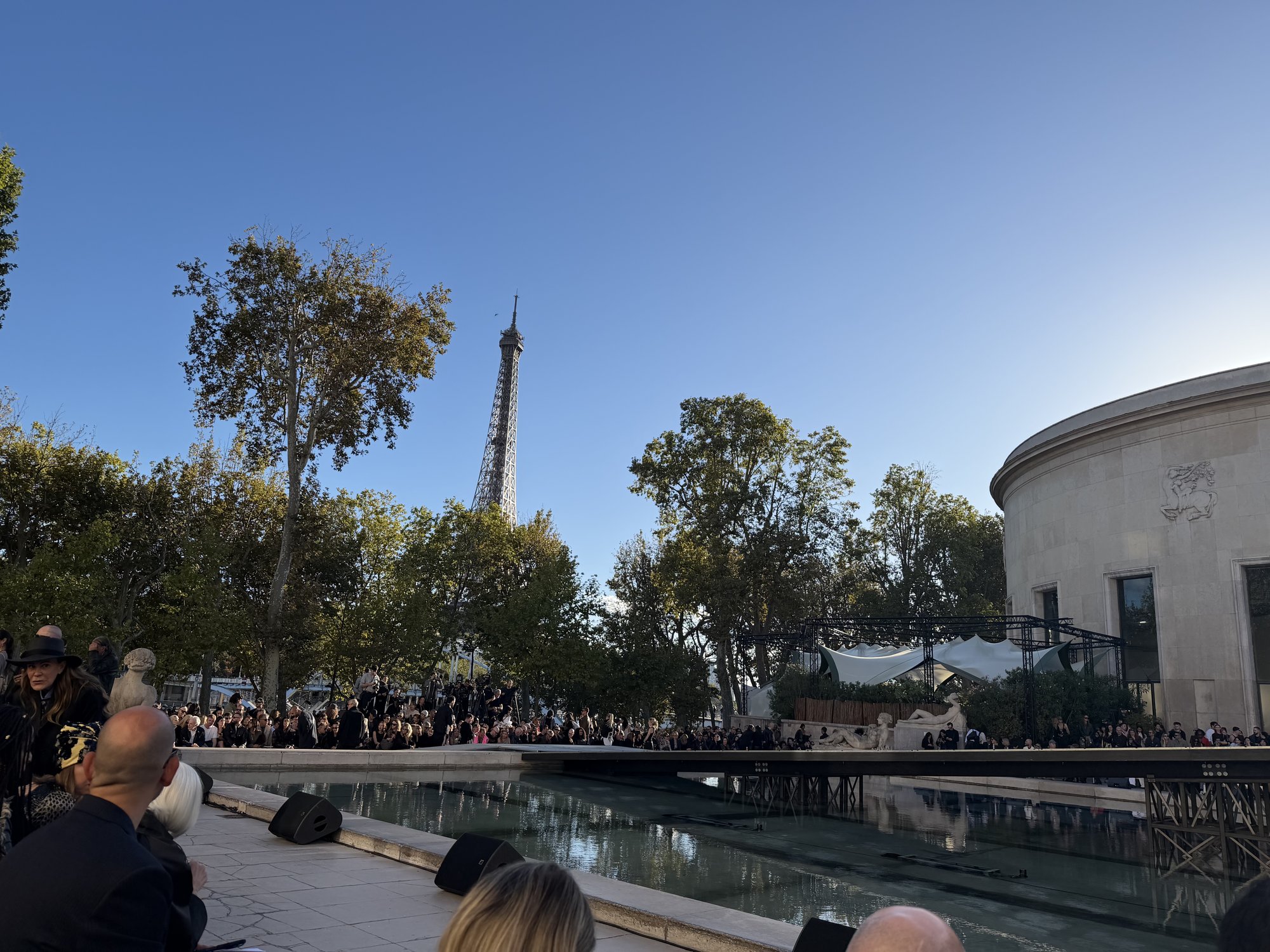 Guests gather around the reflecting pool at the Palais de Tokyo before the Rick Owens show, the Eiffel Tower rising beyond the trees.