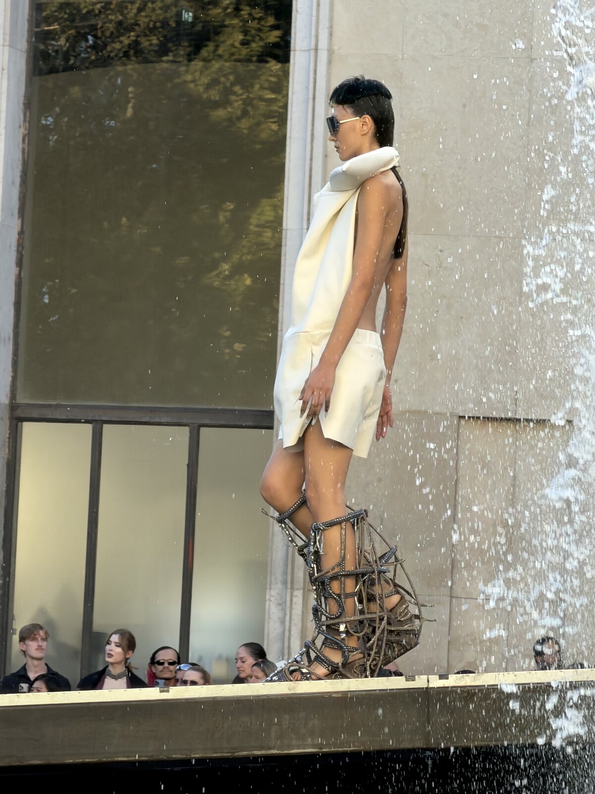 Model in an ivory sculptural look and platform footwear beside a Palais de Tokyo fountain