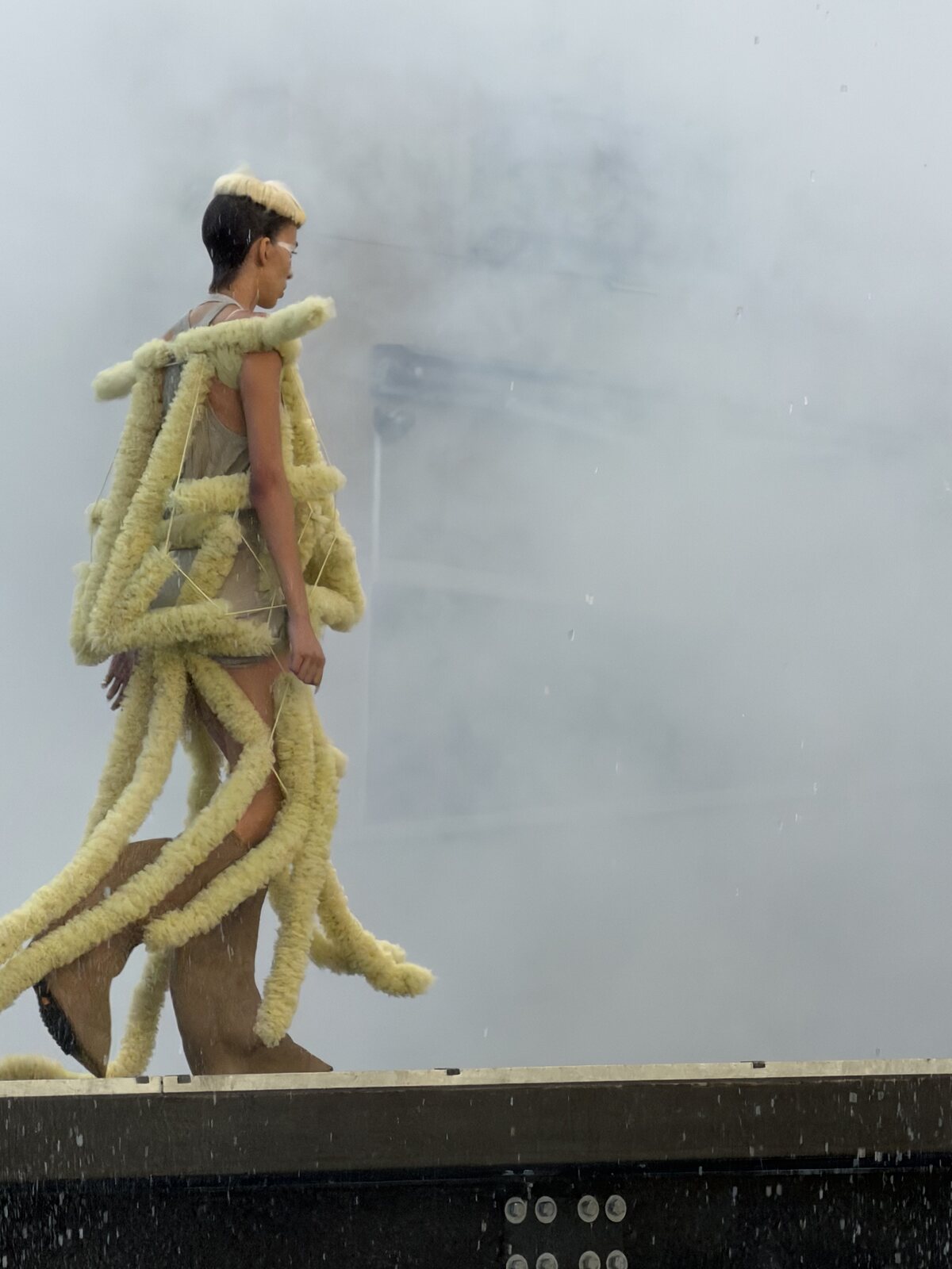 Model in a pale yellow look built from oversized sculptural tubular forms